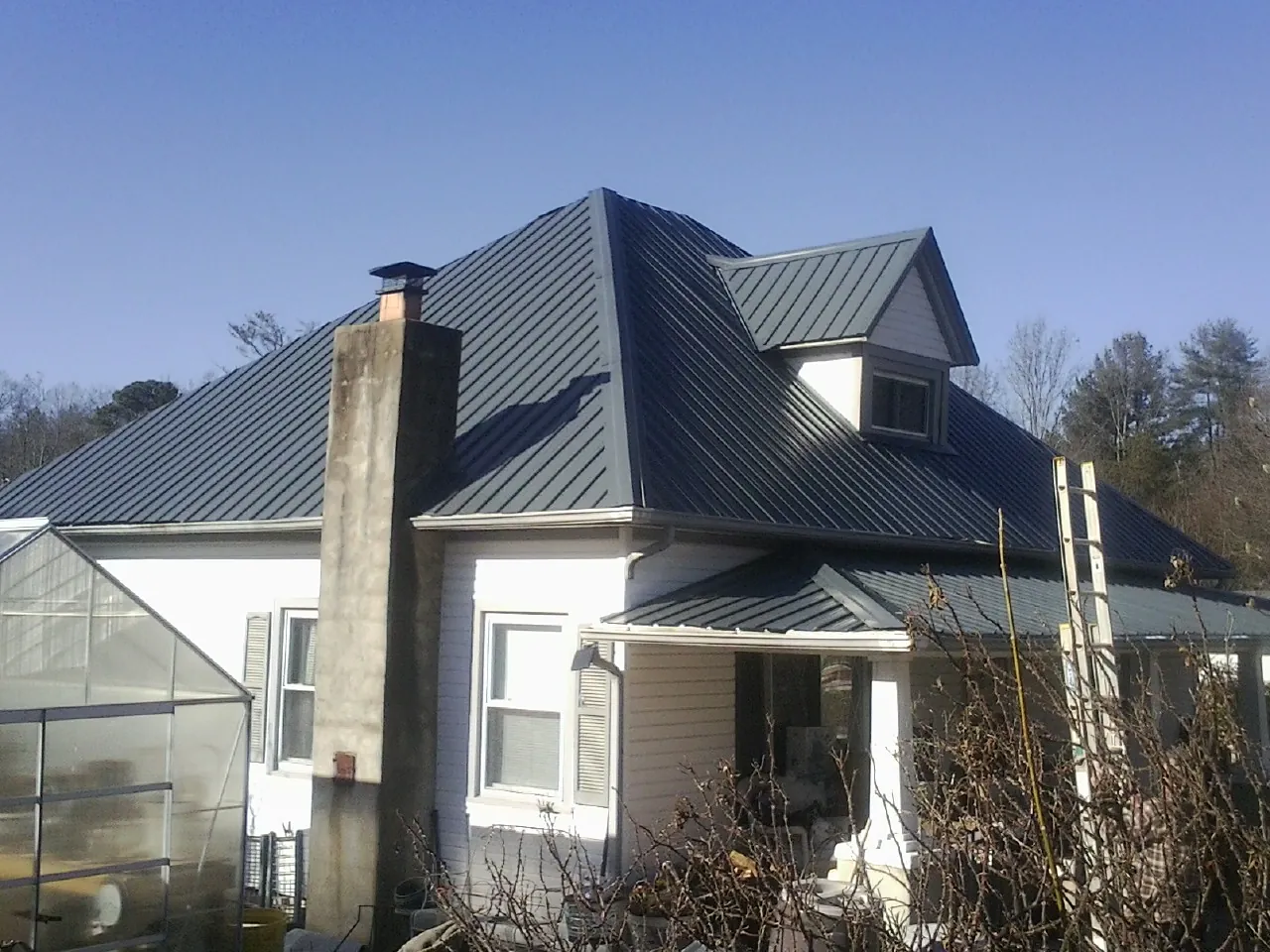 Dark blue standing seam metal roof on a white farmhouse with dormer — Slate & Tile Roof Repair by Roofing Brothers in Box Springs