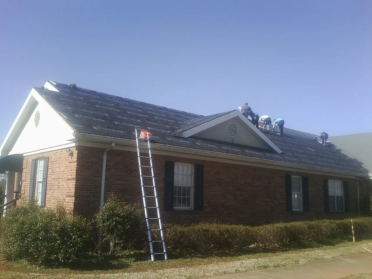Crew tearing shingles off a brick ranch roof with a ladder set — Metal Roof Repair work by our crew in Box Springs