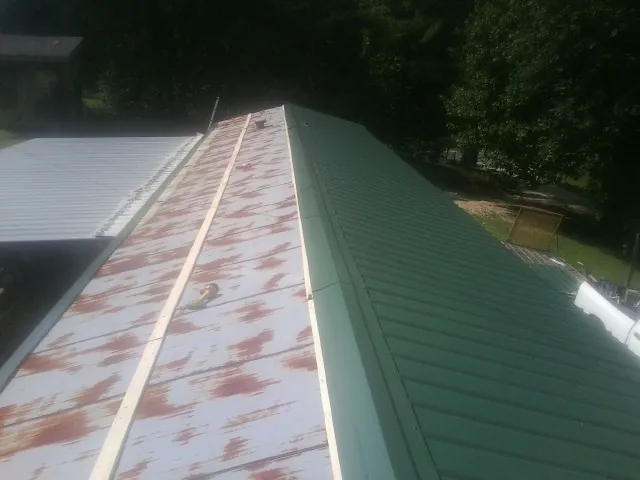 Old rusted panels beside newly installed green metal roofing — Wind Damage Roof Repair by Roofing Brothers in Box Springs