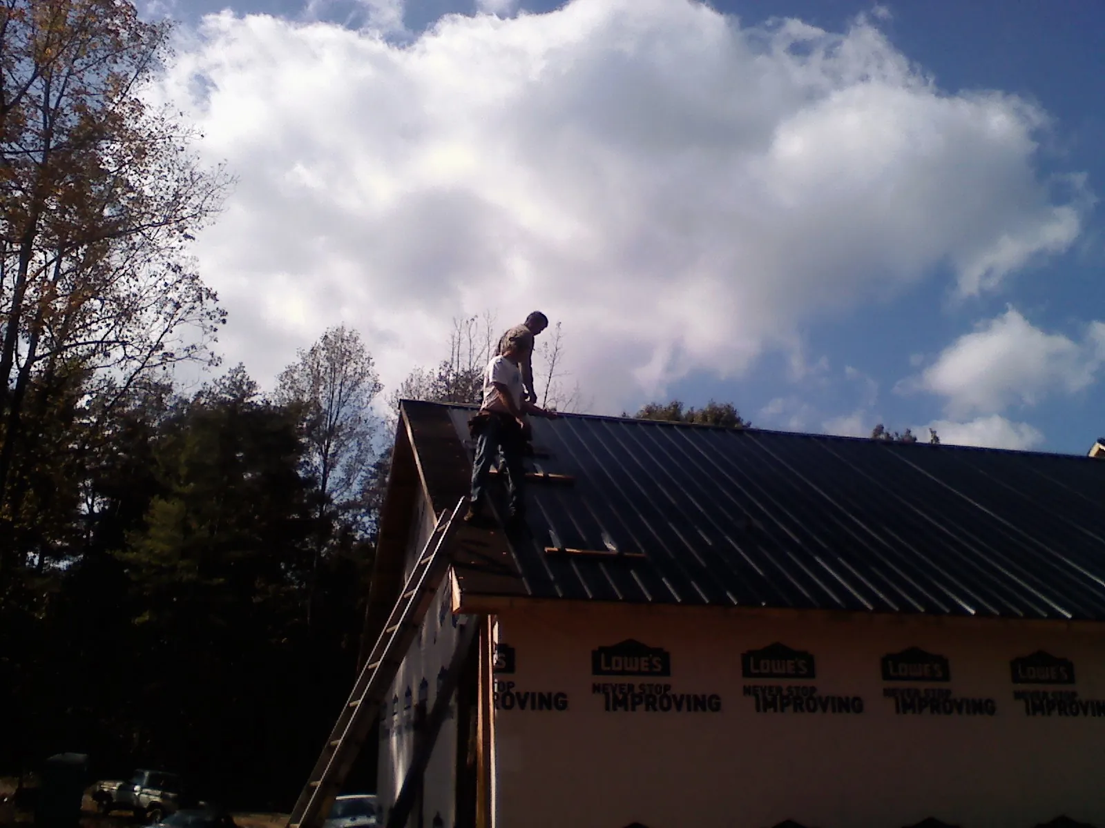 Roofer fastening dark metal panels high against a cloudy sky, from a Roof Inspection job in Box Springs