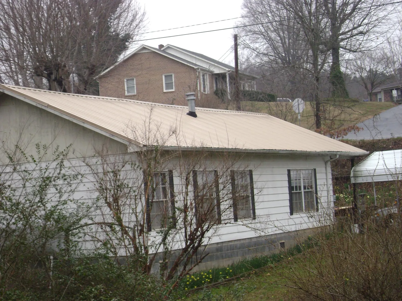 Tan metal roof on a white sided house set into a hillside — Commercial Roofing by Roofing Brothers in Box Springs